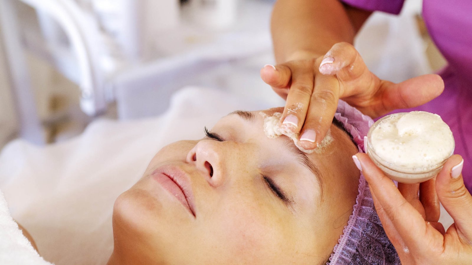 Cosmetologist applies a moisturizing mask on female face. Woman Cosmetologist applies a moisturizing mask on female face. Woman in a spa salon on cosmetic procedures for facial care. White woman getting beauty treatment therapy.