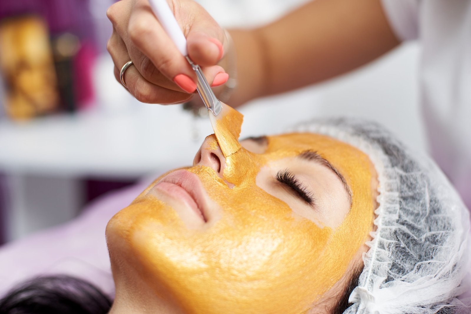 Macro photography of the hand of the beautician with the help of a special brush Macro photography of the hand of the beautician with the help of a special brush puts on the face of the girl a golden mask in the spa