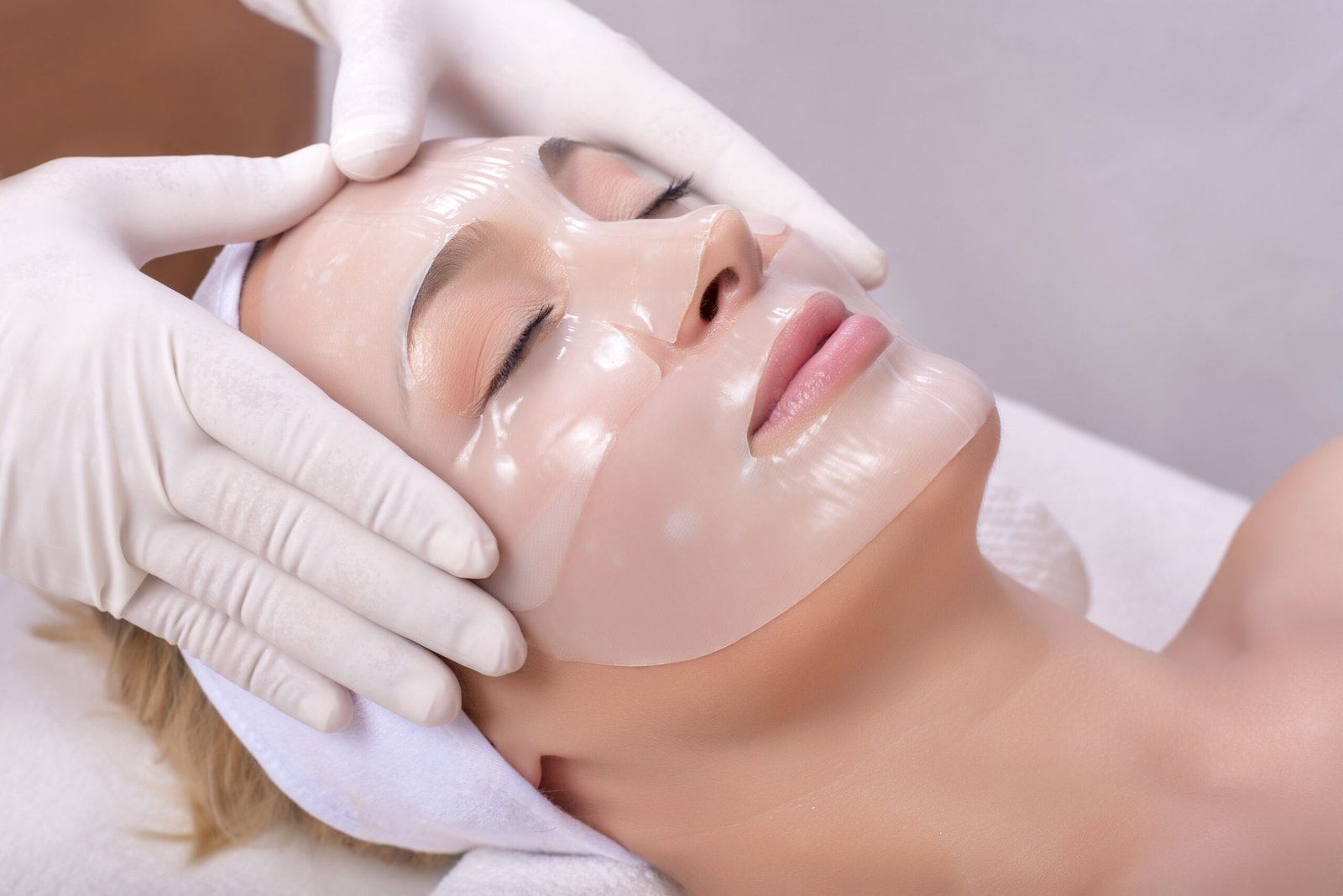 Young female getting skin mask treatment on her face with massage glove A young female getting skin mask treatment on her face with massage glove